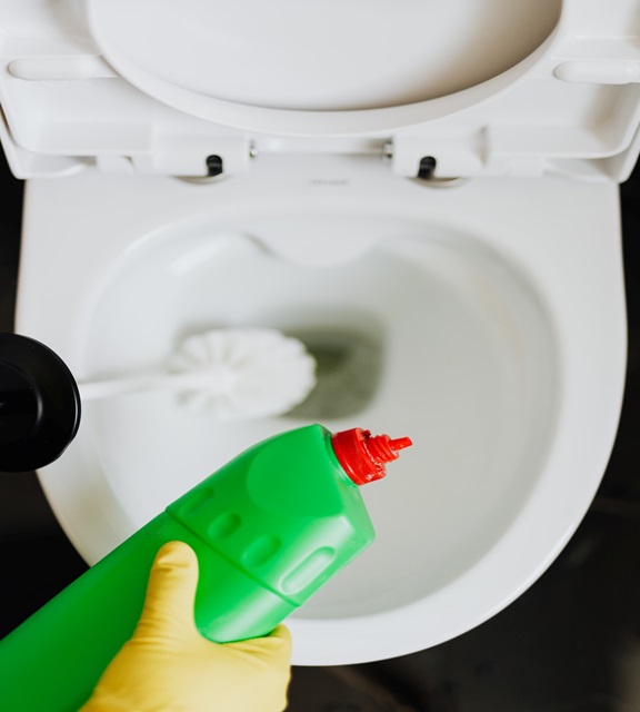 a person holding a cleaning agent over a clogged toilet
