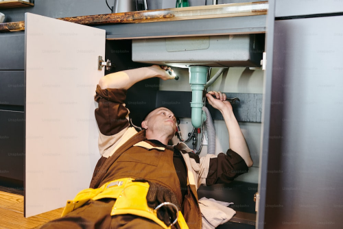 A close-up image of a man fixing a sink pipe with a wrench