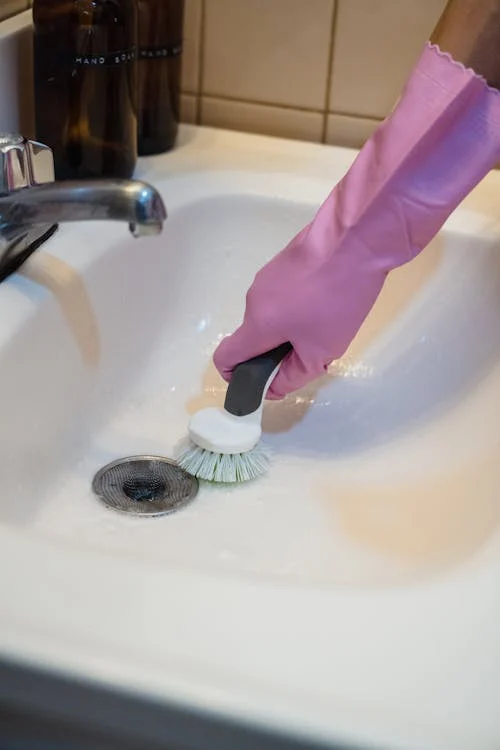 A Person Wearing Pink Glove Cleaning A Bathroom Sink
